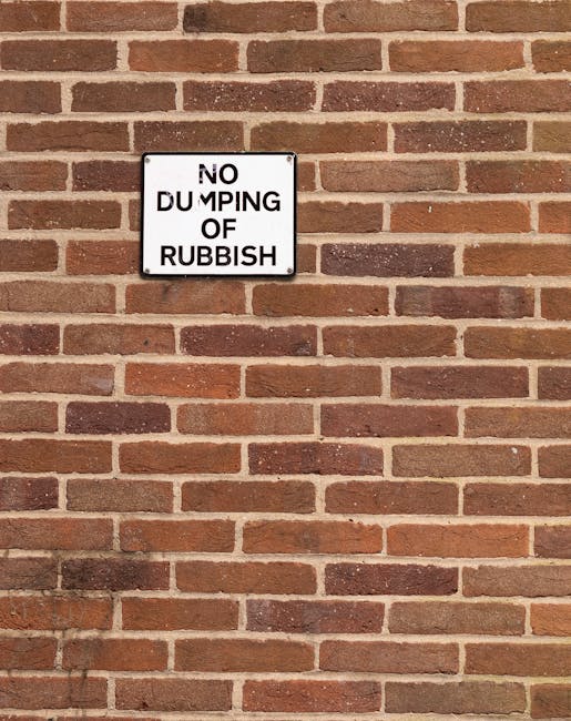 A large outdoor collection of mixed waste and rubbish spilling out from various waste bins on a paved urban street, with some trash overflowing onto the surrounding ground. The scene includes a grey a